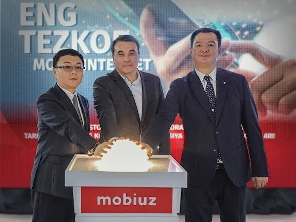 Three men in suits unveil a glowing orb at a Mobiuz event, symbolizing technological advancement.