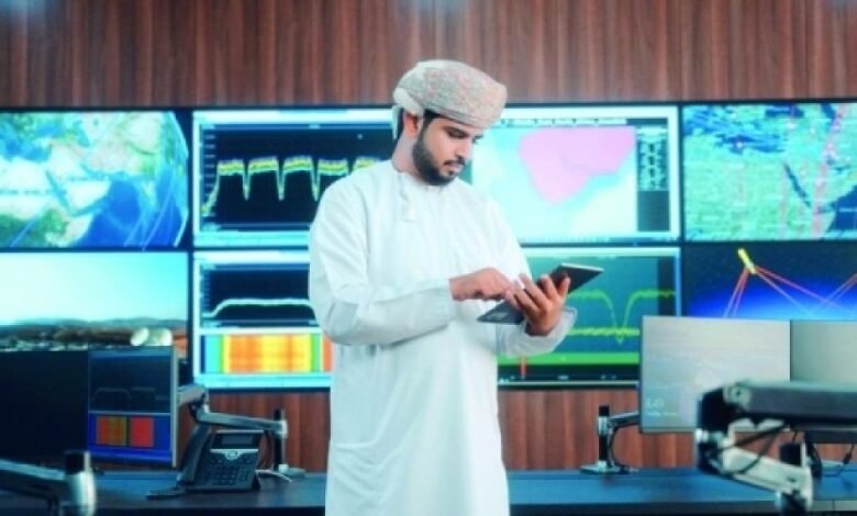 Man in traditional Omani clothing uses tablet in a modern control room with large screens displaying data visualizations.
