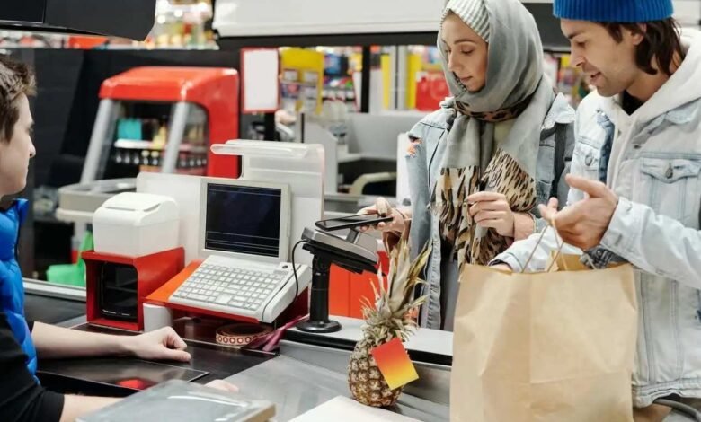 Couple paying with contactless phone at supermarket checkout. Pineapple on counter.
