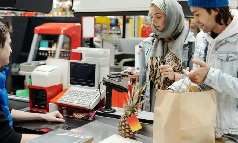 Couple paying with contactless phone at supermarket checkout. Pineapple on counter.