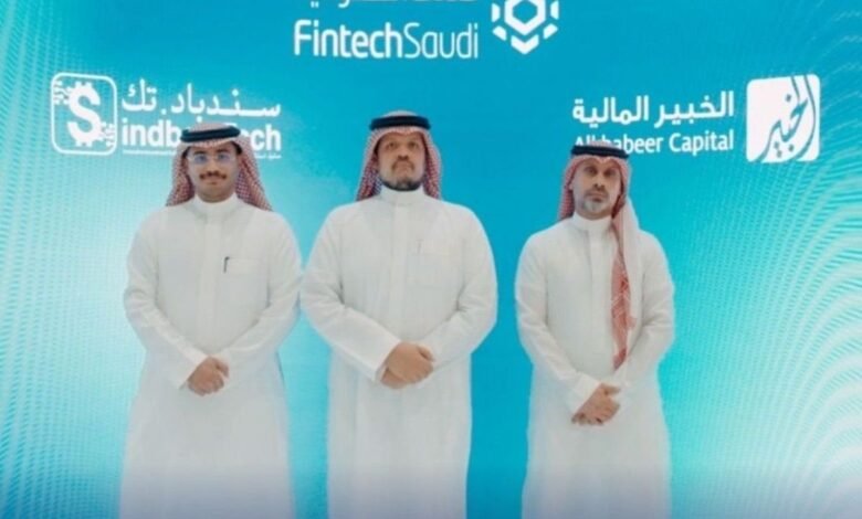 Three men in traditional Saudi Arabian attire stand before a FintechSaudi backdrop.
