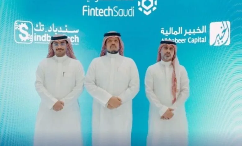 Three men in traditional Saudi Arabian attire stand before a FintechSaudi backdrop.