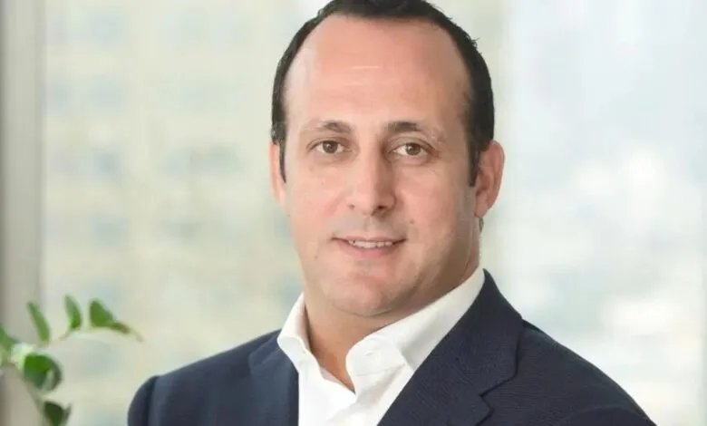 Headshot of a man in a dark suit and white shirt, smiling slightly.