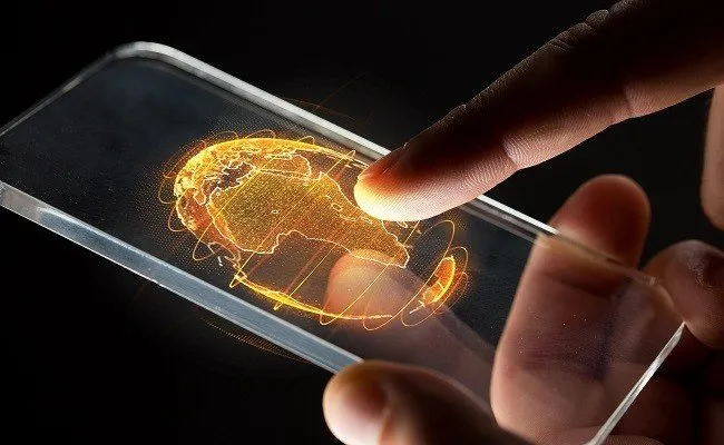 Hand interacts with a transparent phone displaying a glowing orange world map.