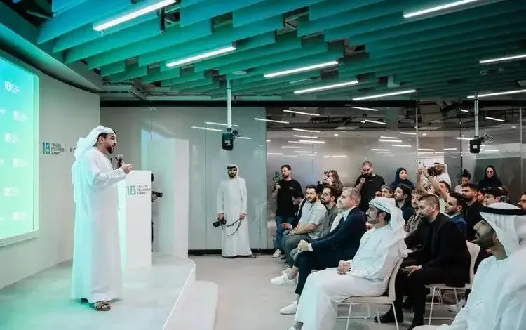 Speaker addressing audience at a modern conference. Teal accents and white attire.