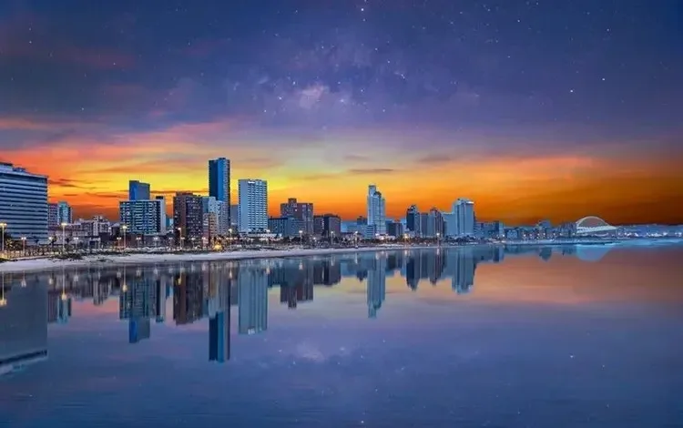 Stunning cityscape at sunset, reflecting in calm water under a starry sky.