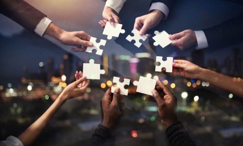 Diverse hands fitting together puzzle pieces against a city backdrop, symbolizing teamwork and collaboration.