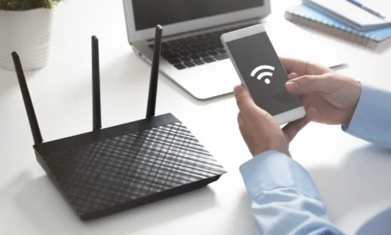 Person holding a smartphone with a Wi-Fi symbol, next to a Wi-Fi router and laptop.