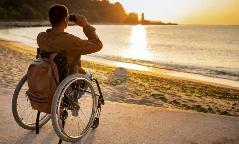 Man in wheelchair on beach looking through binoculars at sunset