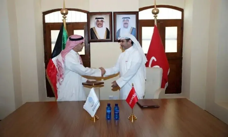 Two men in traditional Arab attire shaking hands in an office with flags and portraits.