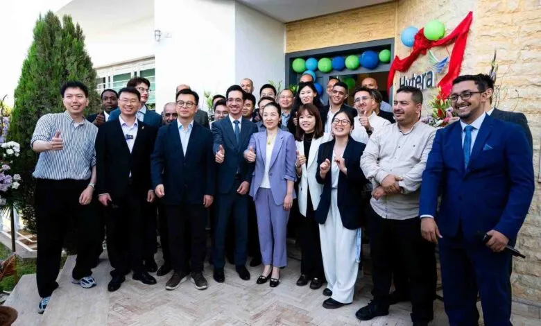 Diverse group of professionals posing for a photo outside a building with balloons and a company logo.