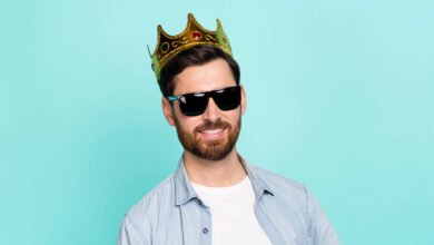 Smiling man wearing sunglasses and a gold crown against a light teal background.