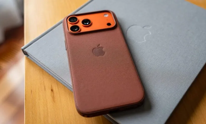 Close-up of a brown iPhone case with an orange camera bump, resting on a grey Apple-branded notebook.