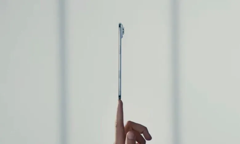 Slim silver smartphone balanced on a fingertip against a light gray background.