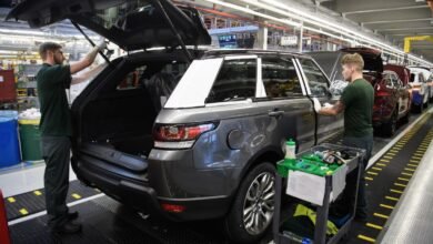 Two workers on an assembly line inspect a dark gray Land Rover Range Rover.