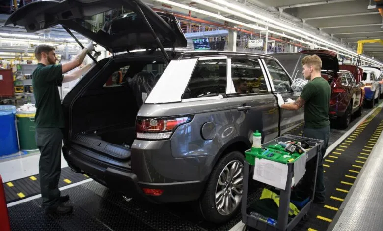 Two workers on an assembly line inspect a dark gray Land Rover Range Rover.