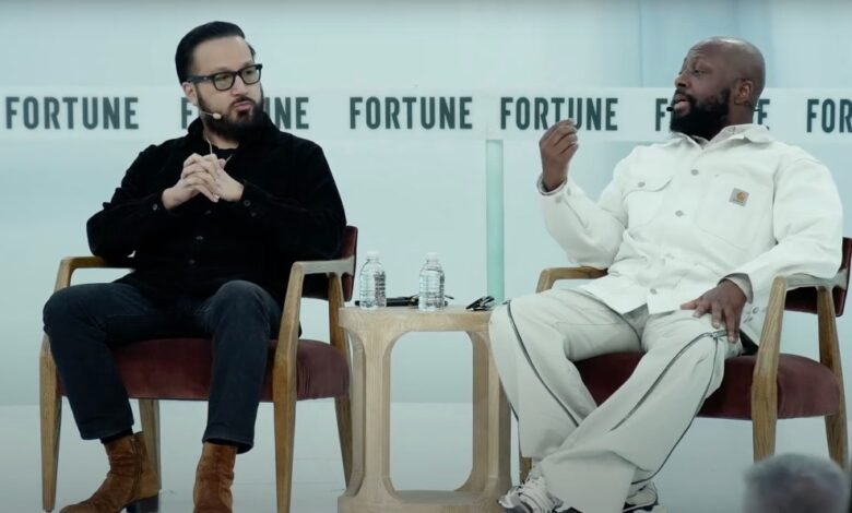 Two men, one in black and one in white, sit in chairs on a stage at a Fortune event, engaged in conversation.