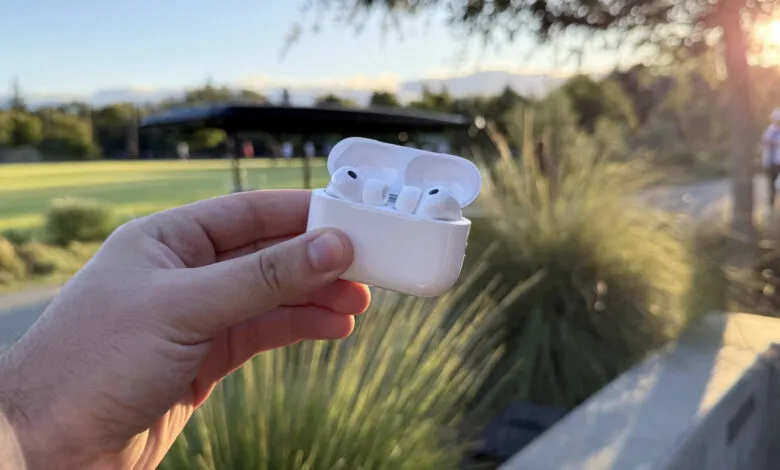 Hand holding open Apple AirPods case outdoors. White earbuds visible.