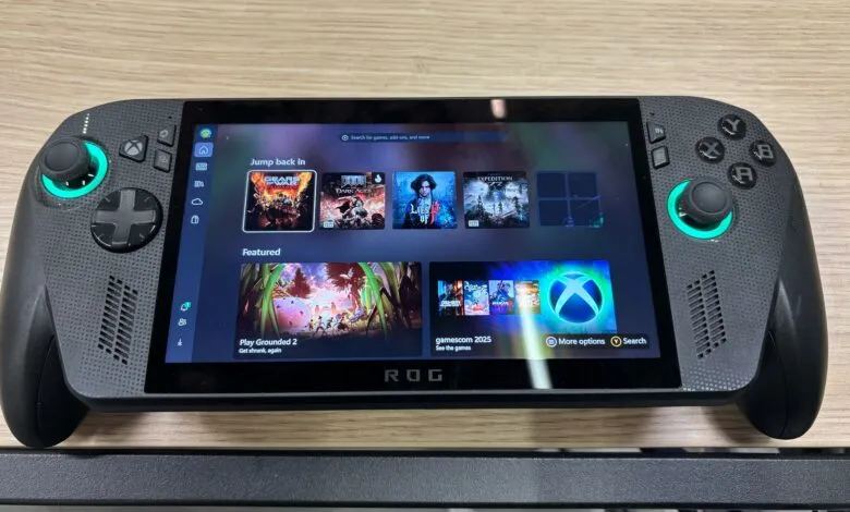 ASUS ROG handheld gaming device displaying various games including Grounded 2 and Doom. Features a dark grey body with teal accents.