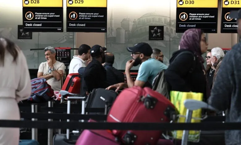 Passengers wait at closed check-in desks at Heathrow Airport. Luggage and signs indicating desk closures are visible.