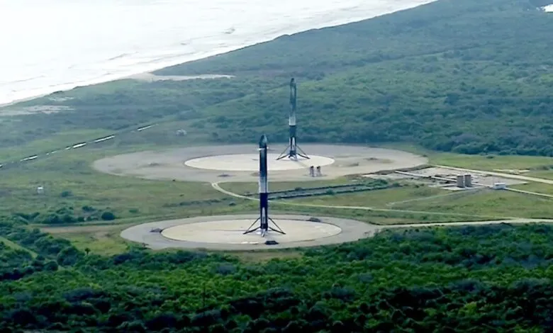 Two SpaceX Starship rockets stand on launchpads near a coastline.