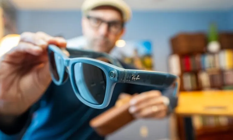 Close-up of a person holding Ray-Ban smart glasses, showcasing the teal frame and subtle branding.