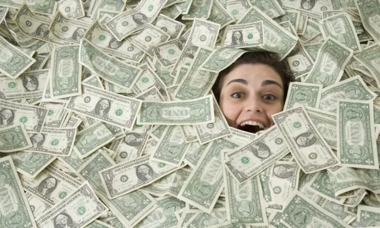 Woman's face emerges from a pile of one-dollar bills, expressing surprise or excitement.