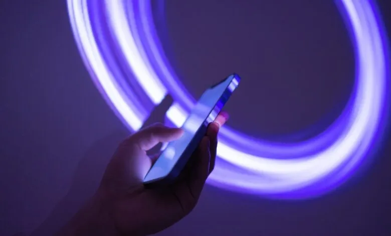 Hand holding a smartphone with a glowing purple light trail behind it.