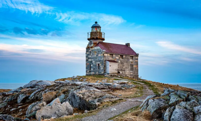 Stone lighthouse on rocky coast under a vibrant blue sky. A tranquil coastal scene.