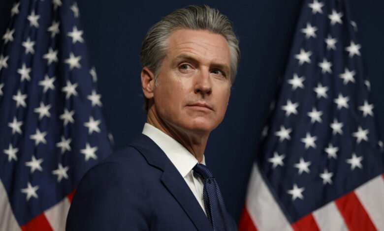 Gavin Newsom, Governor of California, stands between two American flags.