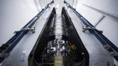 A silver spacecraft inside a large, open metallic structure, possibly in a hangar.