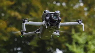 A DJI Mini 5 Pro drone in flight, showcasing its camera and propellers against a blurred green background.
