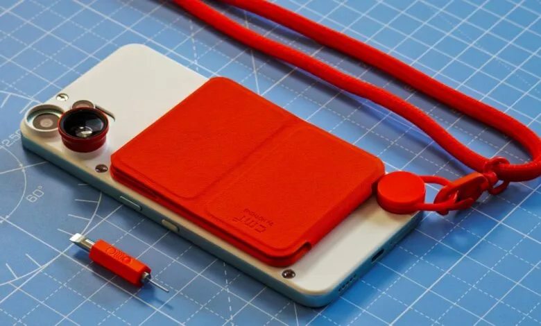 Nothing Phone 2 with red case, lens attachments, and lanyard on a blue cutting mat.