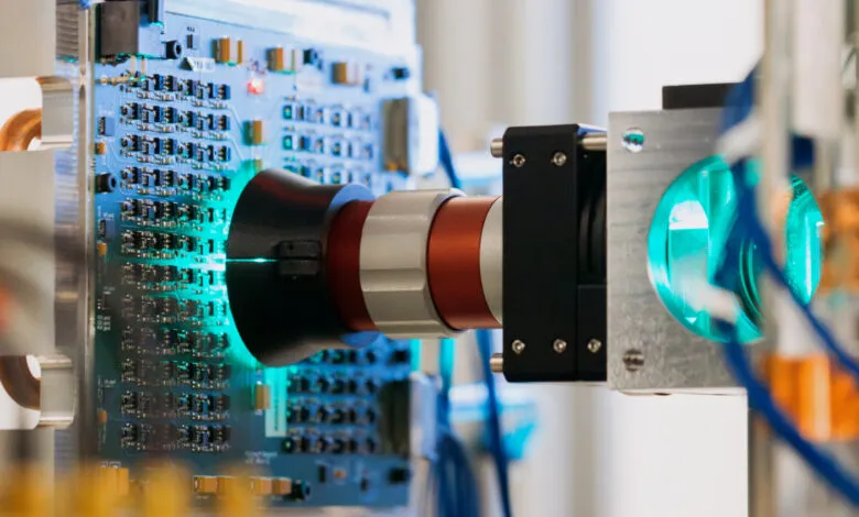 Close-up of advanced technology: a precision instrument inspecting a circuit board with a teal light.