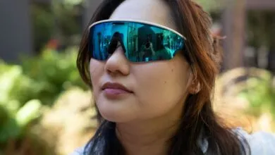 Woman wearing futuristic mirrored blue sunglasses reflecting a photographer and building.