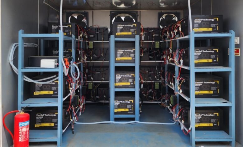 Interior of a container showing numerous ZincGel Technology batteries on shelves, wired together, with cooling fans and a fire extinguisher.