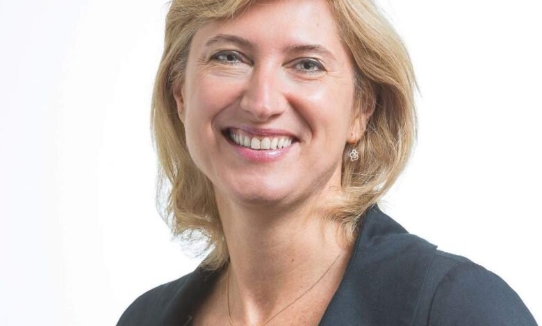 Smiling woman with blonde hair wearing a black jacket against a white background.
