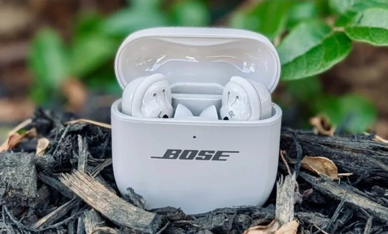 White Bose earbuds in their charging case, resting on dark mulch.