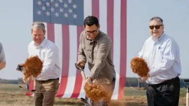 Groundbreaking ceremony with officials and a large American flag in the background.