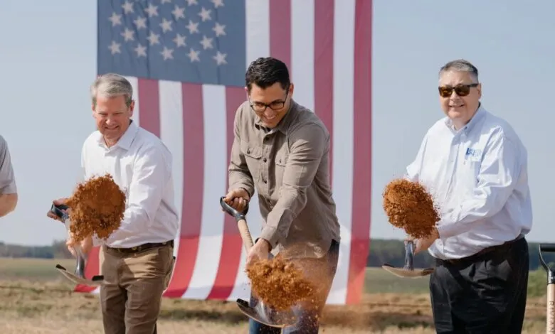 Groundbreaking ceremony with officials and a large American flag in the background.