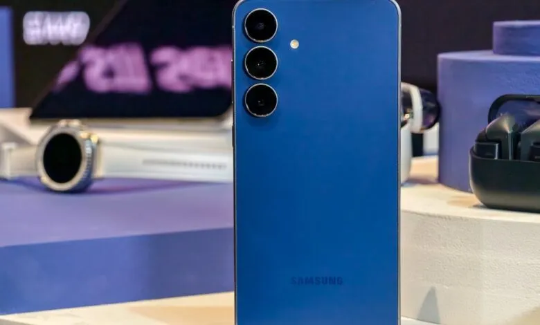 Blue Samsung Galaxy S25 FE smartphone displayed with earbuds and smartwatch.