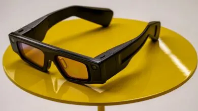 Black Snapchat Spectacles on a yellow table. The glasses have a camera and are sleek and modern.