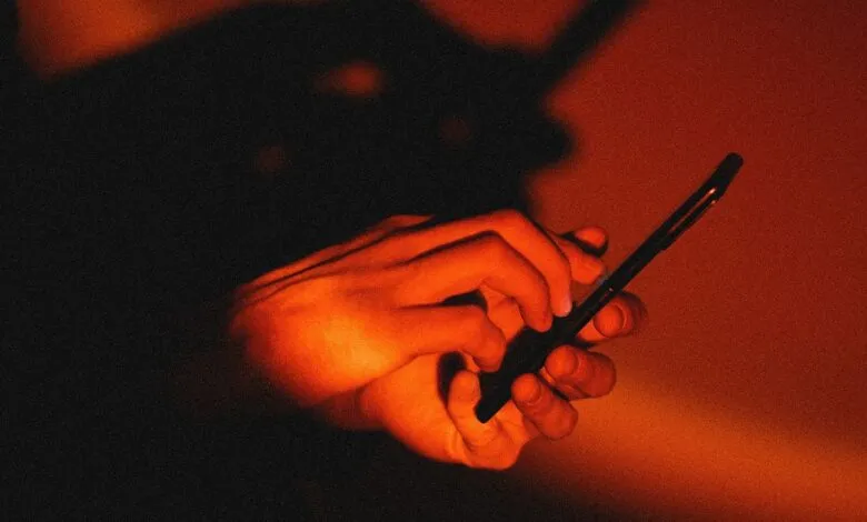 Close-up of hands holding a smartphone, illuminated by warm orange light.