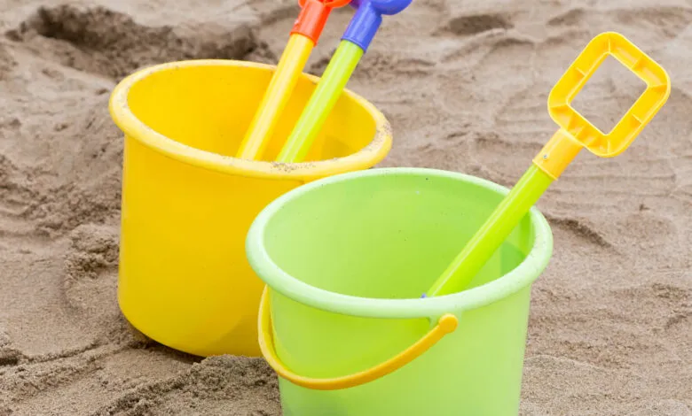 Colorful plastic buckets and shovels sit in the sand at a beach or playground.