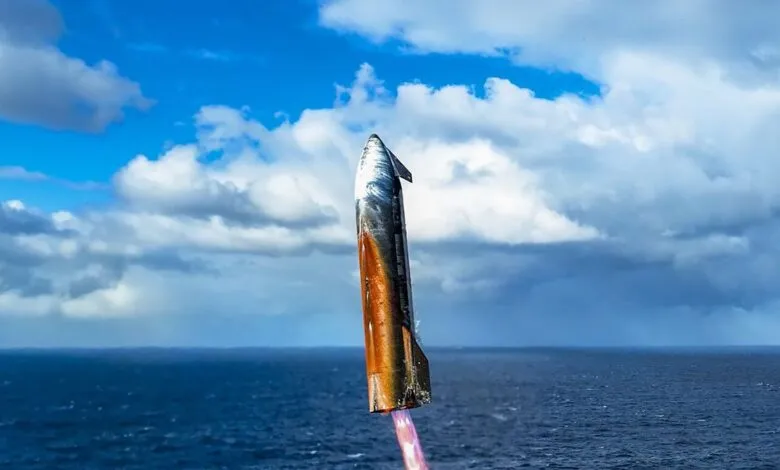 SpaceX Starship prototype ascending over a blue ocean under a partly cloudy sky.