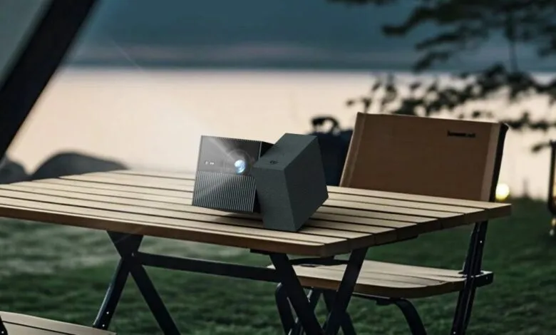 TCL PlayCube projector on outdoor table at dusk, projecting light.