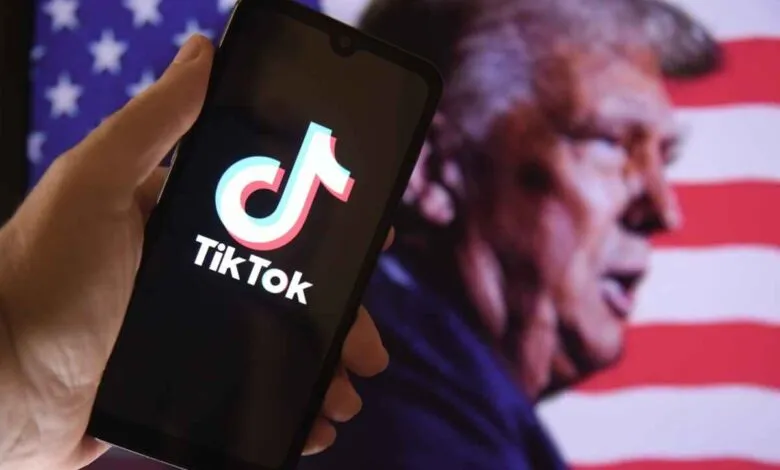 Hand holding a smartphone displaying the TikTok logo with Donald Trump and the US flag in the background.