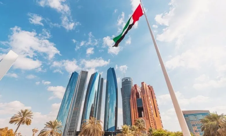 United Arab Emirates flag flying high above modern skyscrapers and palm trees.