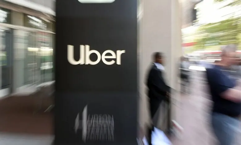 Uber logo on a dark sign, blurred people walking by.
