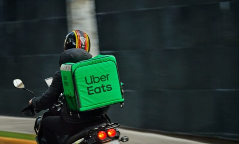 Uber Eats delivery driver on a scooter, wearing a helmet and carrying a bright green insulated bag.